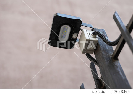LED flashlight connected to residential building communications. Small Black street lamp with twelve diodes fixed to a metal fence outside 117628369