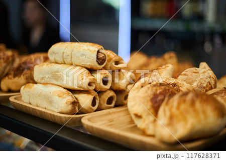 Golden puff pastry baked in oven. Samsa, sausages in dough Varied selection of pastries and snacks in coffee shop. Golden puff pastry baked in oven. Samsa, sausages in dough Varied selection of pastries and snacks in coffee shop. 117628371