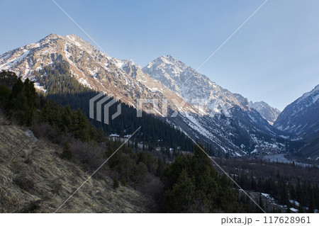 Natural landscape in Ala-Archa National Park, Kyrgyzstan. High rocky mountains in snow, illuminated by warm setting sun 117628961