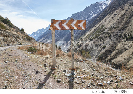 Old traffic sign on the side of the road indicating a left turn in the mountains. 117628962