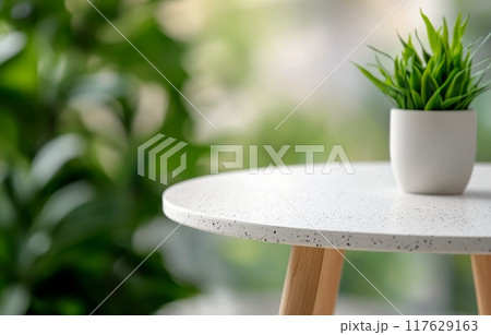 A small potted plant on a light table surrounded by green foliage indoors A small potted plant on a light table surrounded by green foliage indoors 117629163