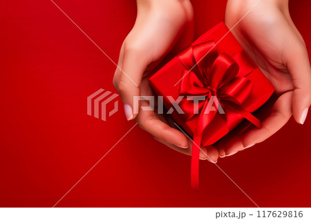 Female hands holding small red gift box with red bow on red background with copy space. 117629816