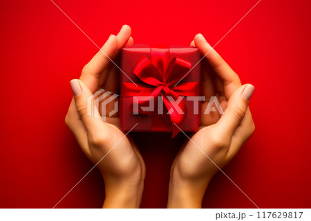 Female hands holding small red gift box with red bow on red background with copy space. 117629817