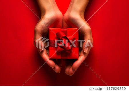 Female hands holding small red gift box with red bow on red background with copy space. 117629820