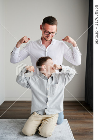 Young father playing with his curious son. Funny kid showing muscles to his dad. Family enjoying activity games at home. 117630858