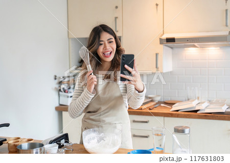 Woman Using Smartphone for Baking Lesson, Culinary Skills in Modern Kitchen 117631803