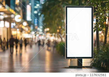 An empty white vertical billboard on the street in the city center with people walking around and green trees and plants 117632561