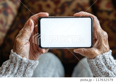 An elderly woman hands holding a smartphone with white screen of the future horizontally in her hands 117632579