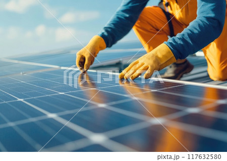 A man in orange pants and a yellow glove is working on a solar panel, green energy and sustainable power technology 117632580
