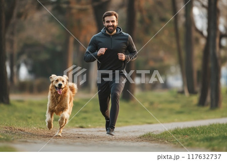 A man and his dog are running together in a park, exercise with pet 117632737