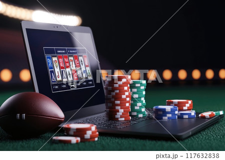 A laptop showing a betting interface, with a football and betting chips scattered around, Online sports betting 117632838