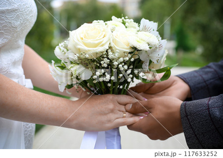 Hands of the bride and groom with a bouquet of roses on a wedding walk, close-up Hands of the bride and groom with a bouquet of roses on a wedding walk, close-up 117633252