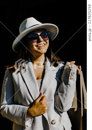 Beautiful brunette businesswoman wearing suit and white hat, walking on the street. 117635259