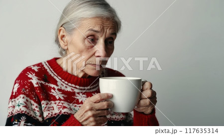 Lonely elderly woman in christmas sweater holding mug and looking sad on white background Lonely elderly woman in christmas sweater holding mug and looking sad on white background 117635314