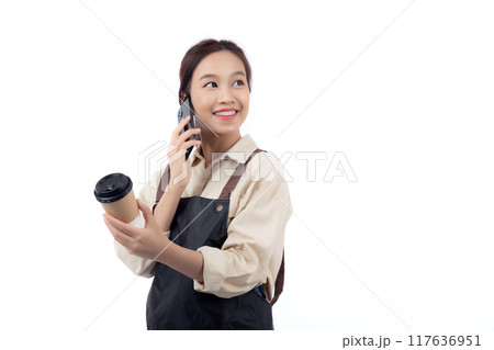 Portrait young asian barista woman wearing apron holding a coffee cup and talking on smartphone. Portrait young asian barista woman wearing apron holding a coffee cup and talking on smartphone. 117636951