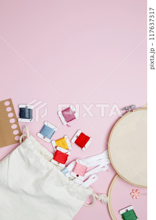 Embroidery set fot stitching. Beige cotton cloth in embroidery hoop on pink background with fabric, colorful threads, scissors and needls Embroidery set fot stitching. Beige cotton cloth in embroidery hoop on pink background with fabric, colorful threads, scissors and needls 117637317