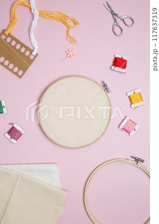 Embroidery set fot stitching. Beige cotton cloth in embroidery hoop on pink background with fabric, colorful threads, scissors and needls 117637319