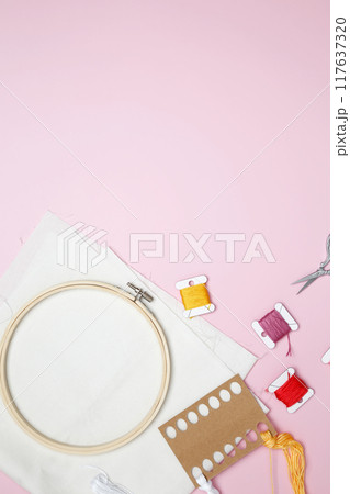 Embroidery set fot stitching. Beige cotton cloth in embroidery hoop on pink background with fabric, colorful threads, scissors and needls 117637320