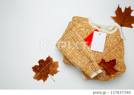 Autumn clothing sales. Warm golden sweater with mock up label. Top view. Copy space Autumn clothing sales. Warm golden sweater with mock up label. Top view. Copy space 117637340