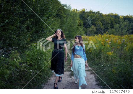 two woman in a whimsical aesthetic style dress in a field in the summer at sunset 117637479