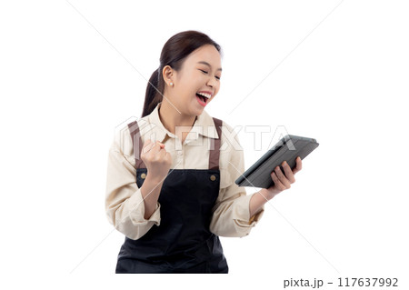 Portrait young asian barista woman wearing an apron celebrating success while using a tablet. Portrait young asian barista woman wearing an apron celebrating success while using a tablet. 117637992