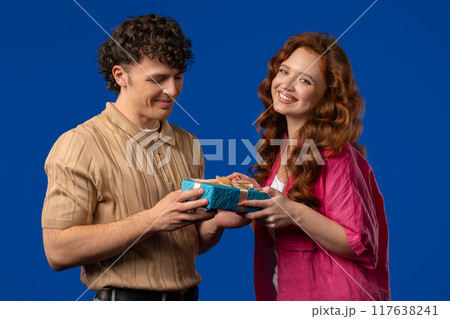 Young woman gives gift box to husband or boyfriend. Surprise, unexpected present. Birthday, celebration, surprise, anniversary concept. Young woman gives gift box to husband or boyfriend. Surprise, unexpected present. Birthday, celebration, surprise, anniversary concept. 117638241