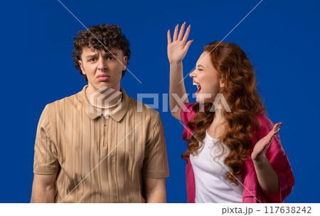 Grumpy woman quarrels on husband or boyfriend On blue. Tired man covers ears 117638242