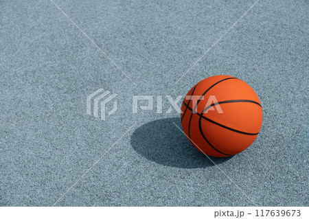 Basketball orange ball with sunny shadow on blue court. Basketball on street or indoor court. Sports gear without people. Template, sport background. Copy space, minimalism. Team sport. 117639673