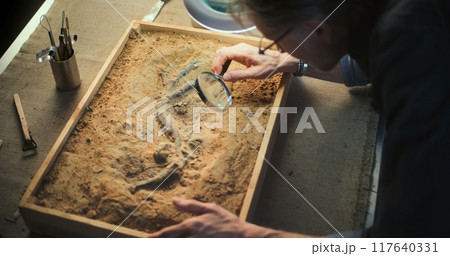 Mature archaeologist does historical bone examination using magnifying glass Mature archaeologist does historical bone examination using magnifying glass 117640331