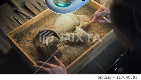 Close up of archaeologist cleaning cultural heritage under lamp, using brush 117640393