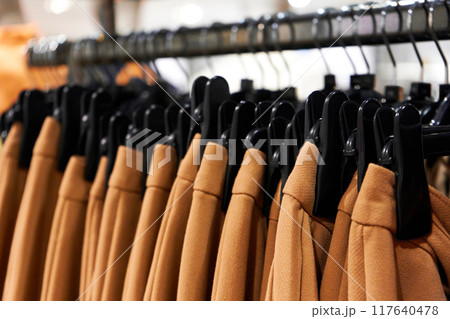 A row of black plastic hangers with identical brown pants in a clothing store. 117640478