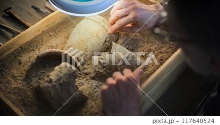 Close up of archaeologist cleaning cultural heritage under lamp, using brush Close up of archaeologist cleaning cultural heritage under lamp, using brush 117640524