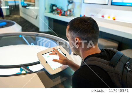 Guy check information about humanoid on tablet. Futuristic science exhibition hall Guy check information about humanoid on tablet. Futuristic science exhibition hall 117640571