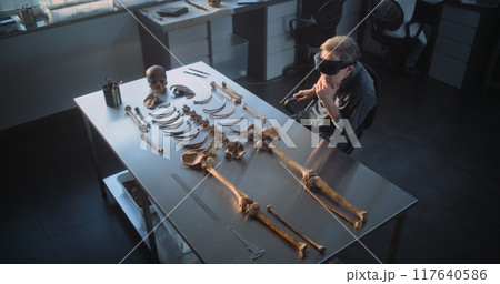 Archaeologist in VR headset does historical research with remains of ancient human 117640586