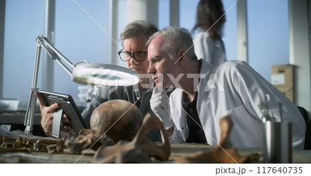 Mature archaeologist uses tablet computer and talks to colleague 117640735