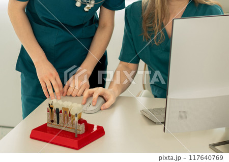 Dentists implantologists look at the computer. On the table there is a model with teeth implants Dentists implantologists look at the computer. On the table there is a model with teeth implants 117640769