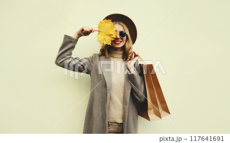 Autumn portrait of beautiful happy woman with shopping bag, stylish girl holding yellow maple leaves 117641691