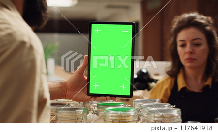 Customer uses mockup tablet in zero waste supermarket to check ingredients for healthy recipe, close up. Client in eco bio local shop with green screen device while shopping for pantry staples 117641918