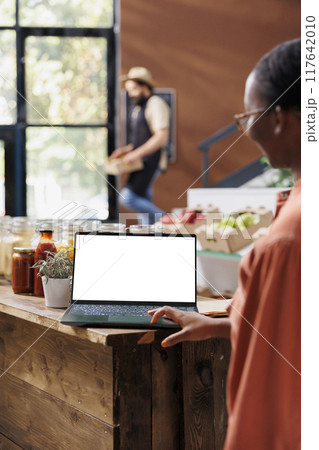 Female customer browsing on laptop with an isolated white screen. African american woman using minicomputer displaying blank chromakey mockup template in an eco friendly sustainable store. Female customer browsing on laptop with an isolated white screen. African american woman using minicomputer displaying blank chromakey mockup template in an eco friendly sustainable store. 117642010