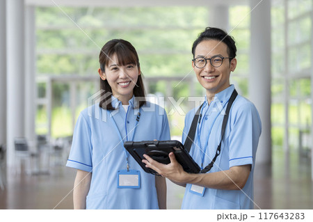 施設職員イメージ　カメラ目線で笑顔のブルーのポロシャツを着た男女 117643283