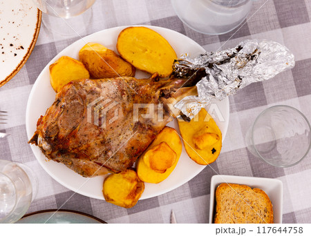 Whole leg of lamb with baked potato on serving table closeup 117644758