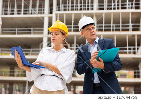 Two architects monitor the progress of work on the construction site, holding a laptop in their hands 117644759