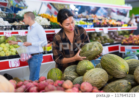 Woman choosing melons in greengrocer Woman choosing melons in greengrocer 117645213