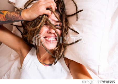 Smiling woman with dreadlocks and tattoos lying on bed. Good morning concept. 117646395