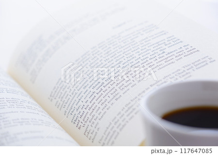 ページを開いた本（洋書）とコーヒーの入ったコーヒーカップで、コーヒーを飲みながら読書を楽しむイメージ 117647085