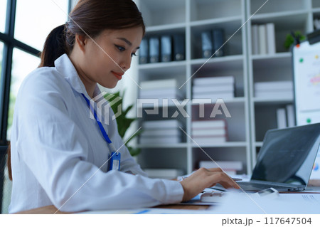 woman meticulously plans a finance audit, using a computer and calculator to review budget documents and ensure accuracy 117647504