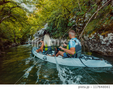 A young couple enjoying an idyllic kayak ride in the middle of a beautiful river surrounded by forest greenery 117648081