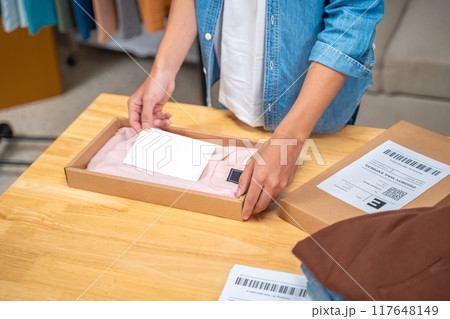 Young online seller man packing his shirt product in the box to ship to his customer from his home studio Young online seller man packing his shirt product in the box to ship to his customer from his home studio 117648149