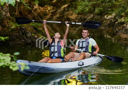 A young couple enjoying an idyllic kayak ride in the middle of a beautiful river surrounded by forest greenery 117648157