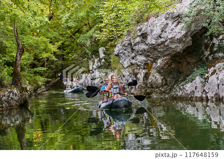 A group of friends enjoying having fun and kayaking while exploring the calm river, surrounding forest and large natural river canyons A group of friends enjoying having fun and kayaking while exploring the calm river, surrounding forest and large natural river canyons 117648159